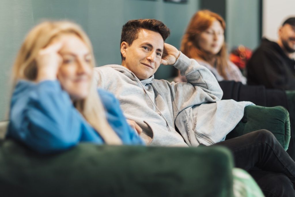 A casual group meeting indoors with several adults sitting on a sofa and engaging in conversation.